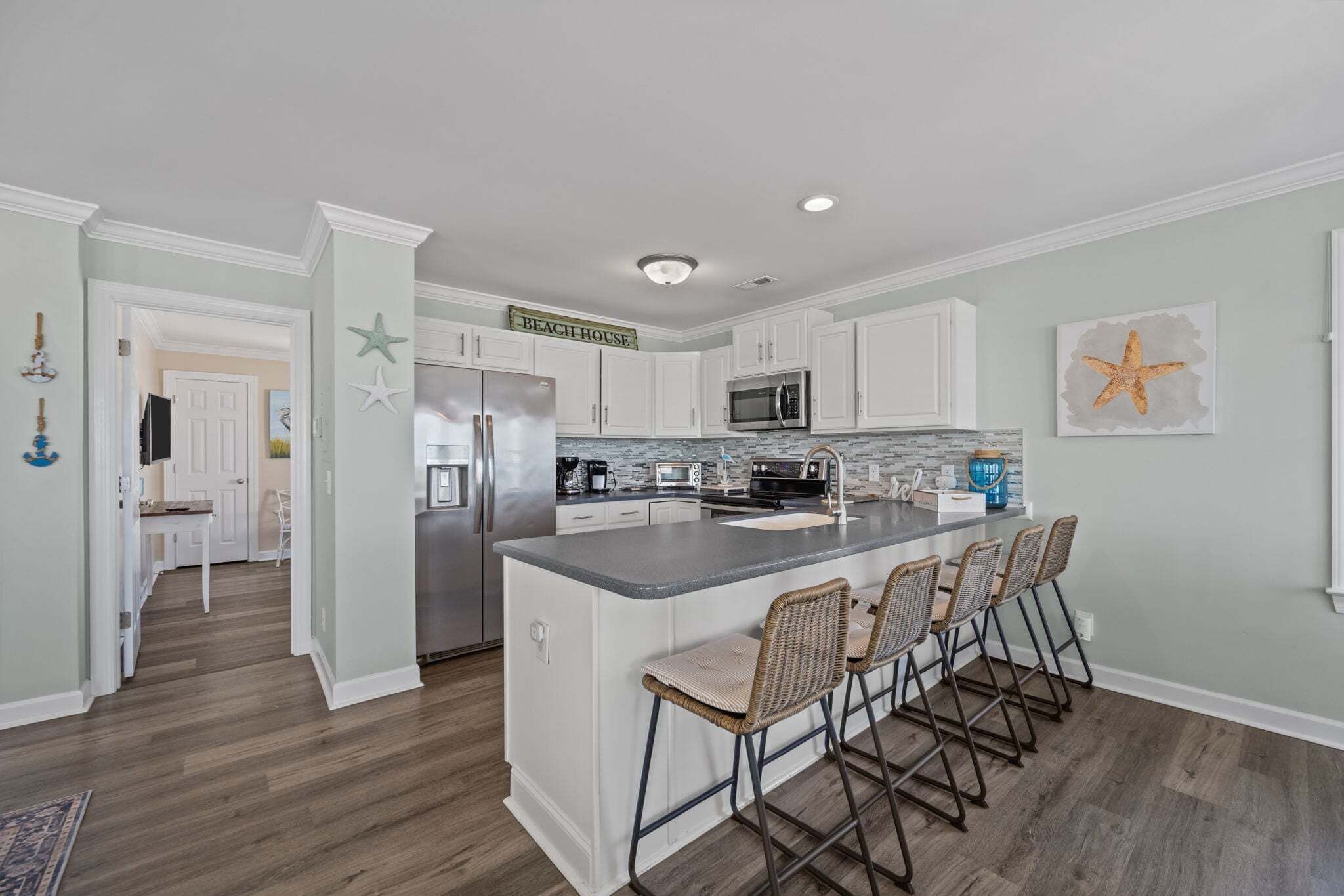 A kitchen with white cabinets, a central island with bar stools, a microwave, and a refrigerator.