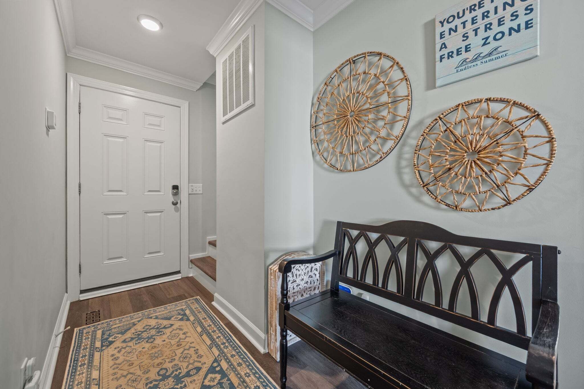 A hallway with a white door, a bench, and two wall decorations.