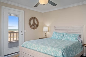Une chambre à coucher avec un lit, un ventilateur de plafond, une porte donnant sur la plage et un élément décoratif mural.