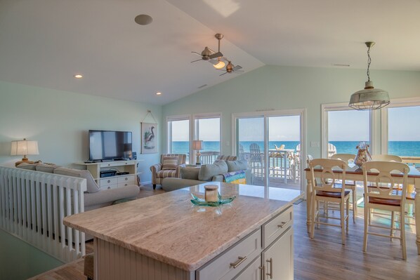 A spacious living area with a large TV, comfortable seating, a kitchen island, and a view of the ocean. - A Little Coastal Sass, Stunning Ocean Views & Beach Days at Your Doorstep! (North Topsail Beach)