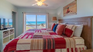 Quarto com cama grande, ventoinha no teto, televisão e vista para a praia.
