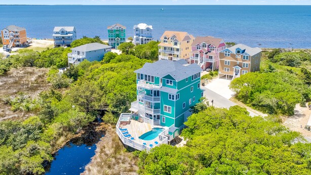 Zona residencial costera con varias casas de varios pisos, una piscina y una playa al fondo.