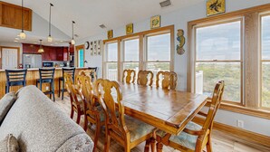 Un comedor con mesa y sillas de madera, una cocina al fondo y grandes ventanas con vistas.