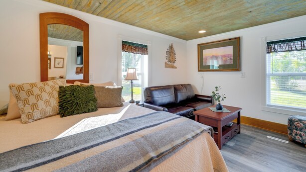 A bedroom with a large bed, a wooden ceiling, a mirror, a window with blinds, a sofa, and a small table with a vase. - Pet-Friendly Farmhouse Suite w/ Patio in Vaughn! (Vaughn)