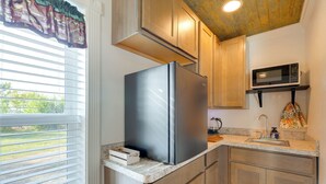 A compact kitchen with a stainless steel refrigerator, a microwave, wooden cabinets, a sink, and a window with blinds. - Pet-Friendly Farmhouse Suite w/ Patio in Vaughn! (Vaughn)