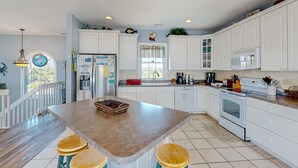 A kitchen with white cabinets, a central island with stools, a refrigerator, a microwave, and a sink. - Beachfront home with pool, private hot tub, beach access & lovely views (North Topsail Beach)