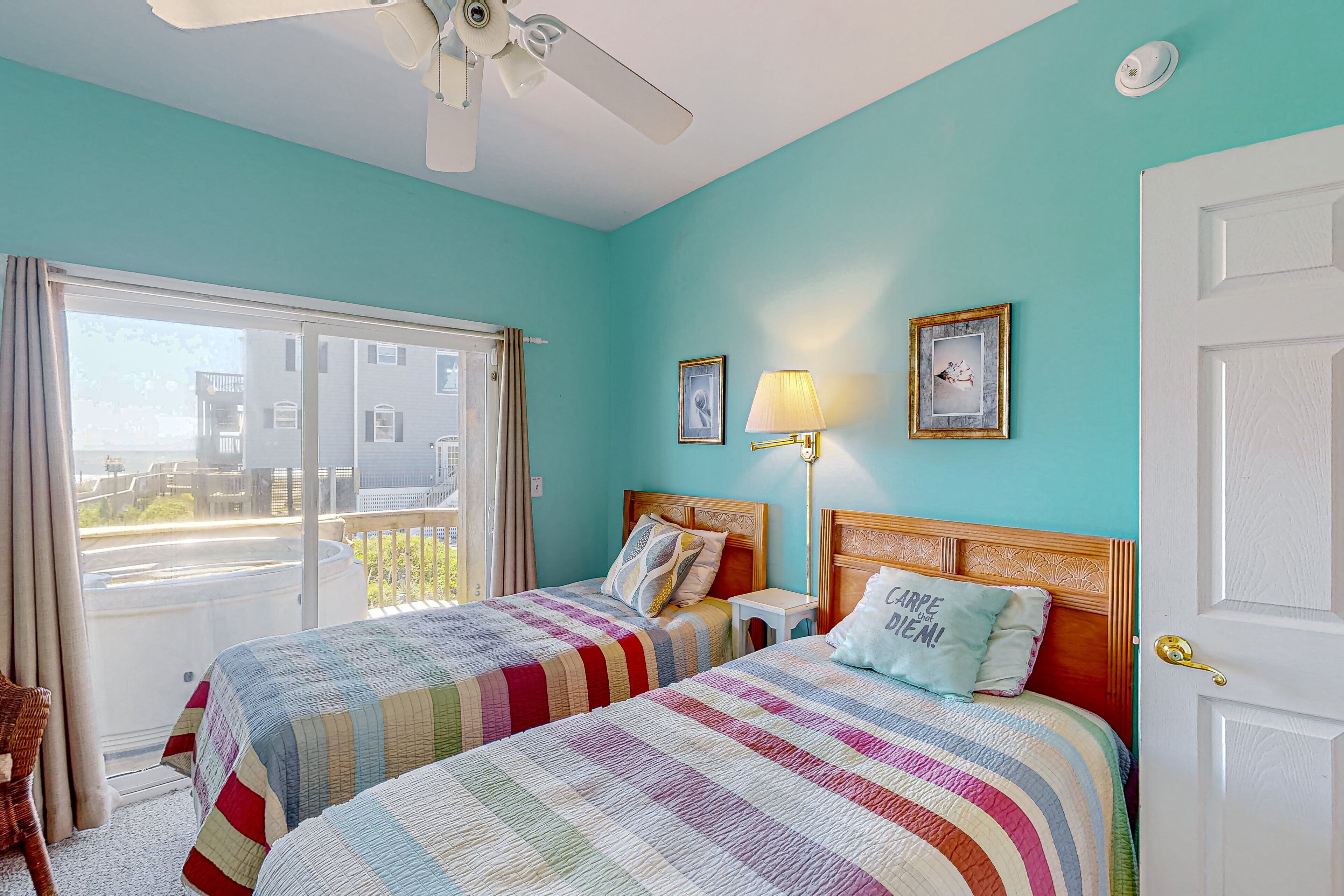A room with two beds, a ceiling fan, a window with curtains, and a door.