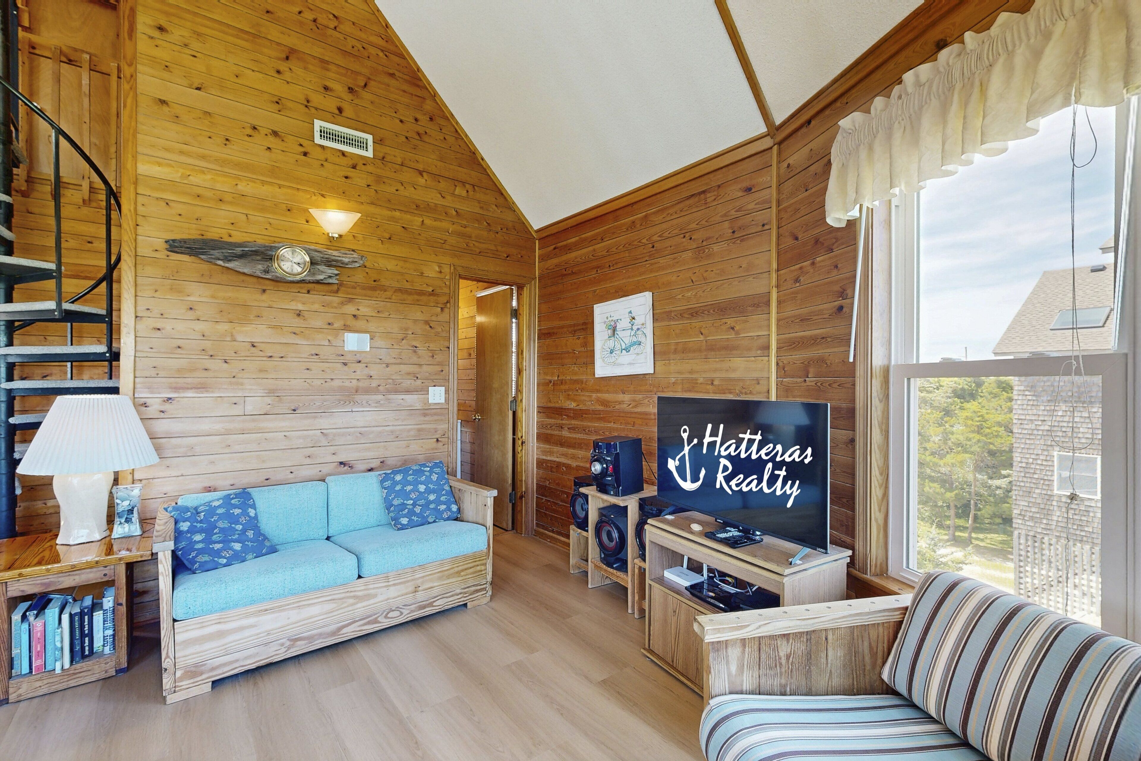 A cozy cabin-style room with a wooden interior, a sofa, a television, and a bookshelf.