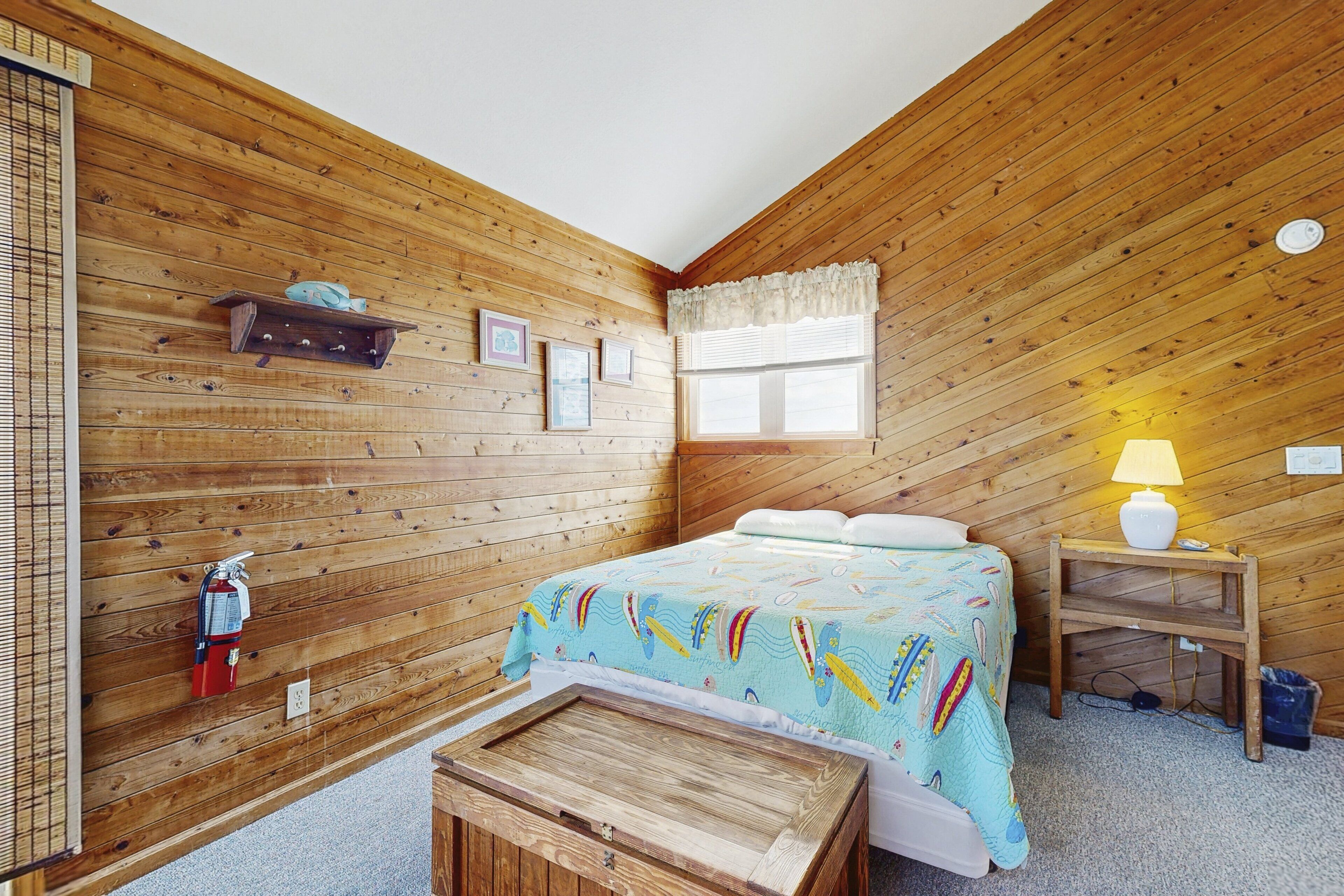 Una camera in legno con un letto, un tavolino, una lampada, uno scaffale con un pesce e un estintore.