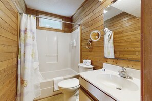 A bathroom with wooden paneling, a shower, a toilet, a sink, and a mirror. - Sandy Paws 394: Stunning Views, Pool Access, Pet-Friendly (Avon)