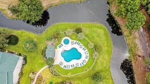 Luchtbeeld van een resort met een centraal gelegen zwembad, omringd door keurig onderhouden gazons en bomen.
