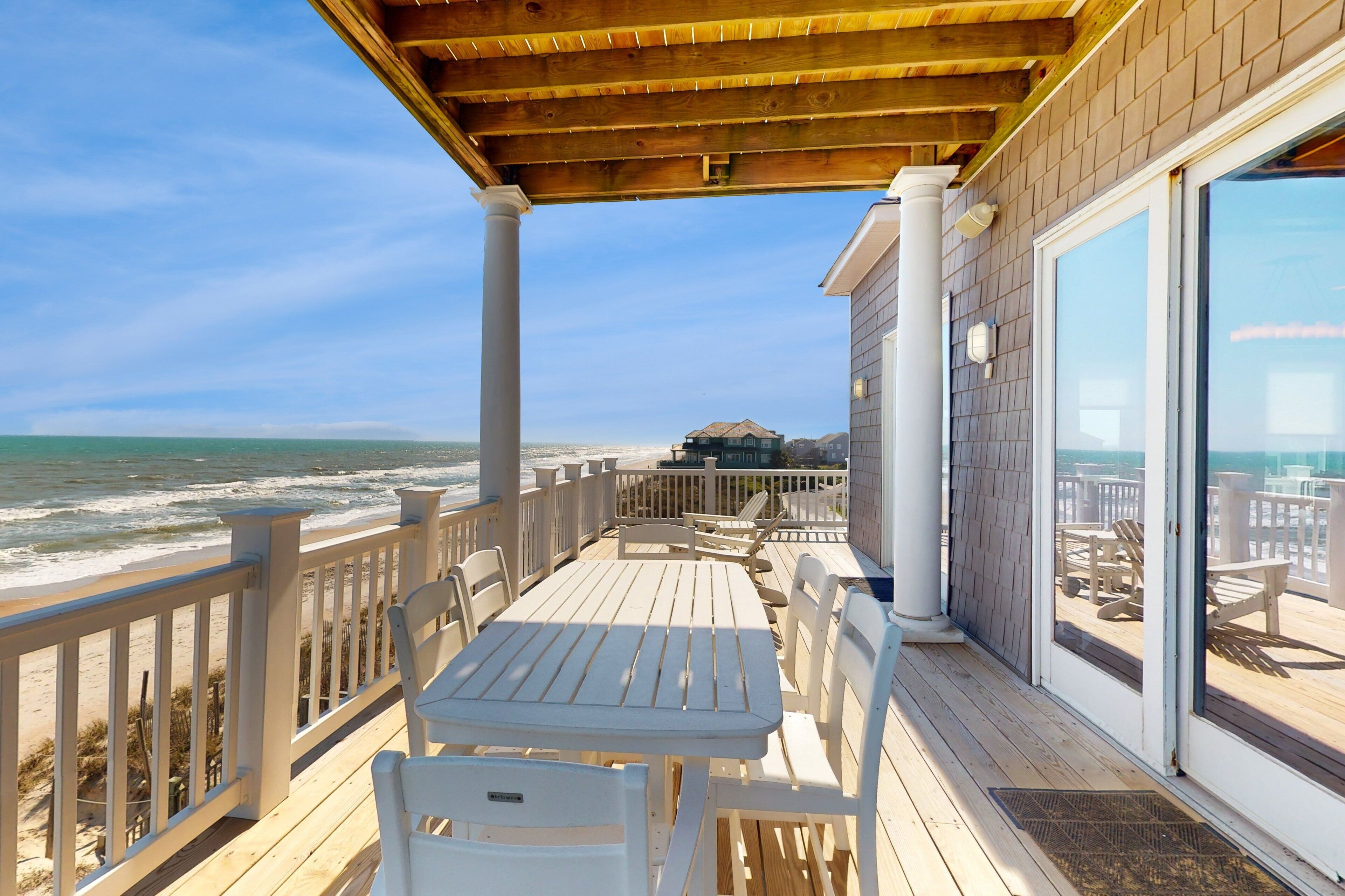 Une terrasse en bois avec une table et des chaises, donnant sur l’océan.