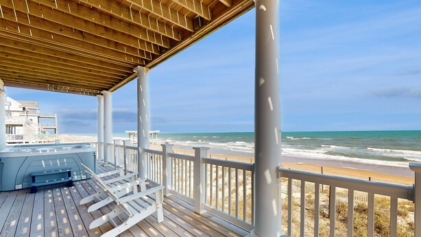 Un pontile in legno con idromassaggio, ringhiere bianche e vista sulla spiaggia e sull'oceano.