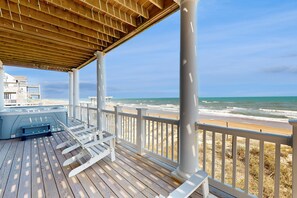 Une terrasse en bois dotée d’un jacuzzi, de rampes blanches et offrant une vue sur la plage et l’océan.