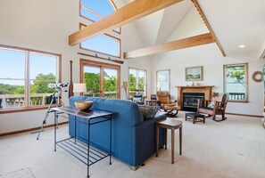 A spacious living room with a blue sofa, a fireplace, and large windows offering a view of the outdoors.