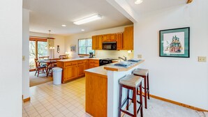 A modern kitchen with wooden cabinets, a central island, and a dining area with chairs. - Canalfront home with a deck, sound access, central AC, WiFi, washer/dryer (Frisco)