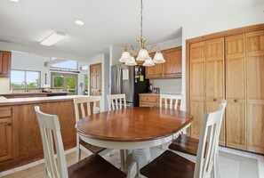 A modern kitchen with a central island, wooden cabinets, and a round dining table with chairs.