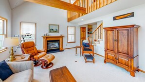 A spacious living room with a high ceiling, a fireplace, a large wooden cabinet, and a staircase leading to an upper level. - Canalfront home with a deck, sound access, central AC, WiFi, washer/dryer (Frisco)