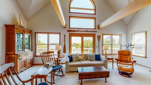 A spacious living room with a high ceiling, large windows, a wooden cabinet, a sofa, a rocking chair, and a coffee table. - Canalfront home with a deck, sound access, central AC, WiFi, washer/dryer (Frisco)