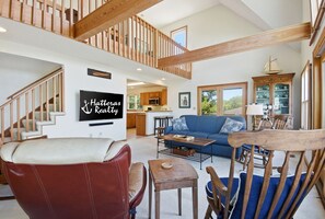 Un vaste espace de vie comprenant un escalier, un canapé, une table basse et un téléviseur diffusant des images de « Hatteras Realty ».