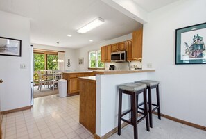 A modern kitchen with wooden cabinets, a central island, and bar stools. - Canalfront home with a deck, sound access, central AC, WiFi, washer/dryer (Frisco)