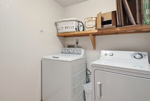 A laundry room with a washing machine and dryer, a shelf with books and a basket, and a wall socket. - Canalfront home with a deck, sound access, central AC, WiFi, washer/dryer (Frisco)