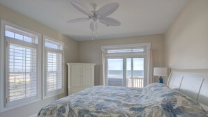 Un dormitorio con una cama grande, un ventilador de techo y vista al océano a través de las ventanas.