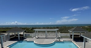 A swimming pool with a view of the ocean, surrounded by a wooden deck and covered structures. - Beachfront home with beach access, pool, private hot tub & ocean views (North Topsail Beach)