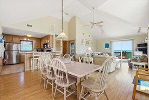 A spacious living area with a dining table, chairs, a sofa, and a balcony with a view.