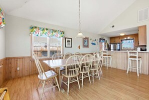 A dining area with a wooden table and chairs, a kitchen with a refrigerator and stove, and a window with blinds.