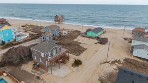 Luchtbeeld van een pand aan het strand met meerdere huizen, een houten terras en een zwembad.