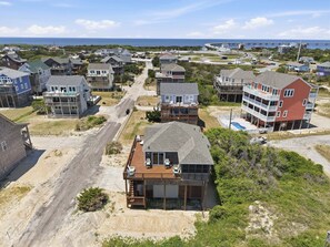 A coastal residential area with houses, a road, and a bridge in the background.