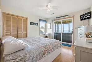 A bedroom with a bed, a ceiling fan, a sliding glass door to a balcony, a sign reading 'Hatteras Realty,' and a 'PEACH' sign on the wall.