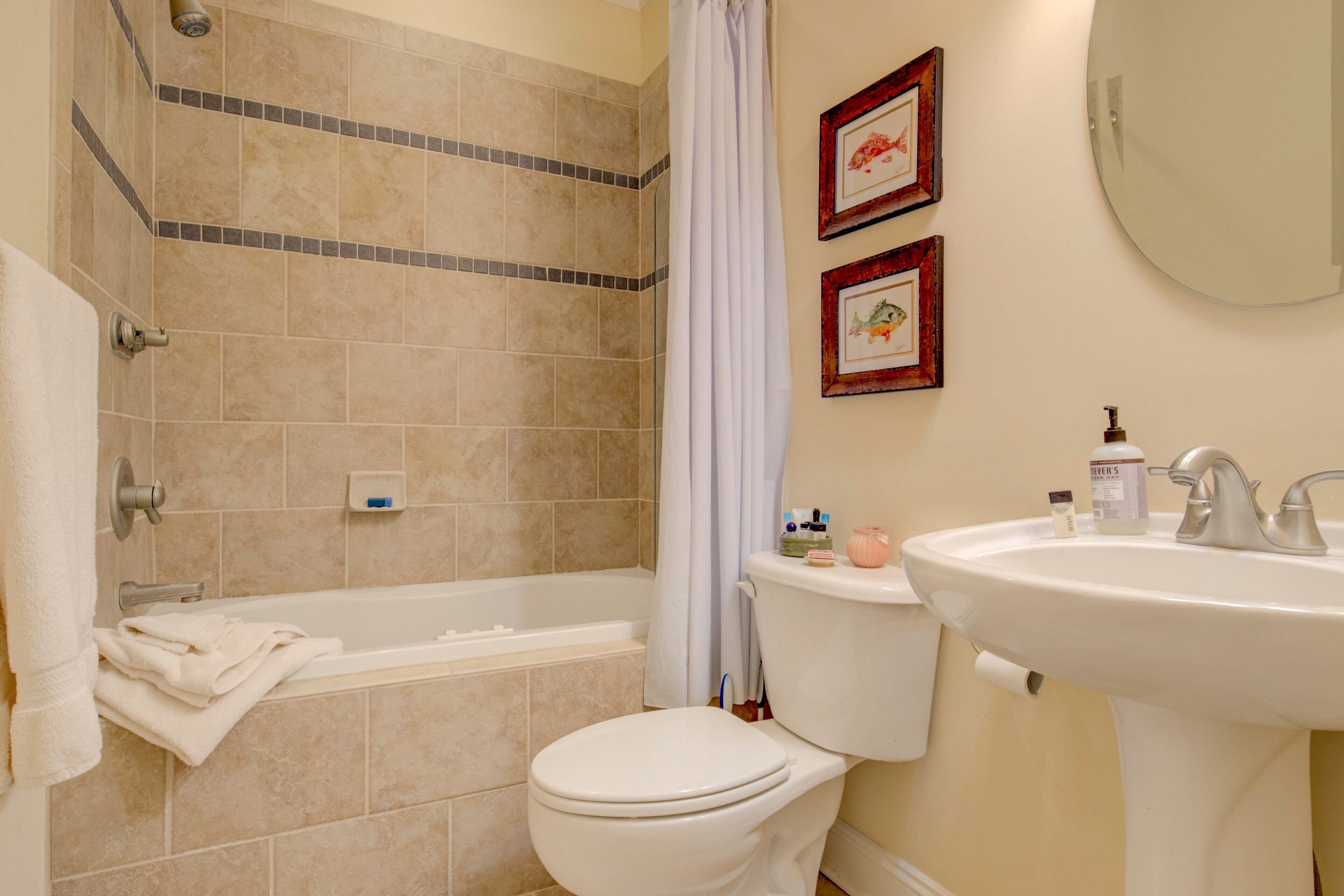 Une salle de bain avec une baignoire, des toilettes, un lavabo et deux tableaux encadrés au mur.