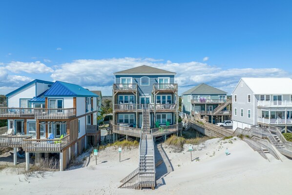 A beachfront property with multiple buildings, including a central two-story house with a balcony and a staircase leading to a deck. - Oceanfront home with beach access, hot tub, washer/dryer & central AC (North Topsail Beach)