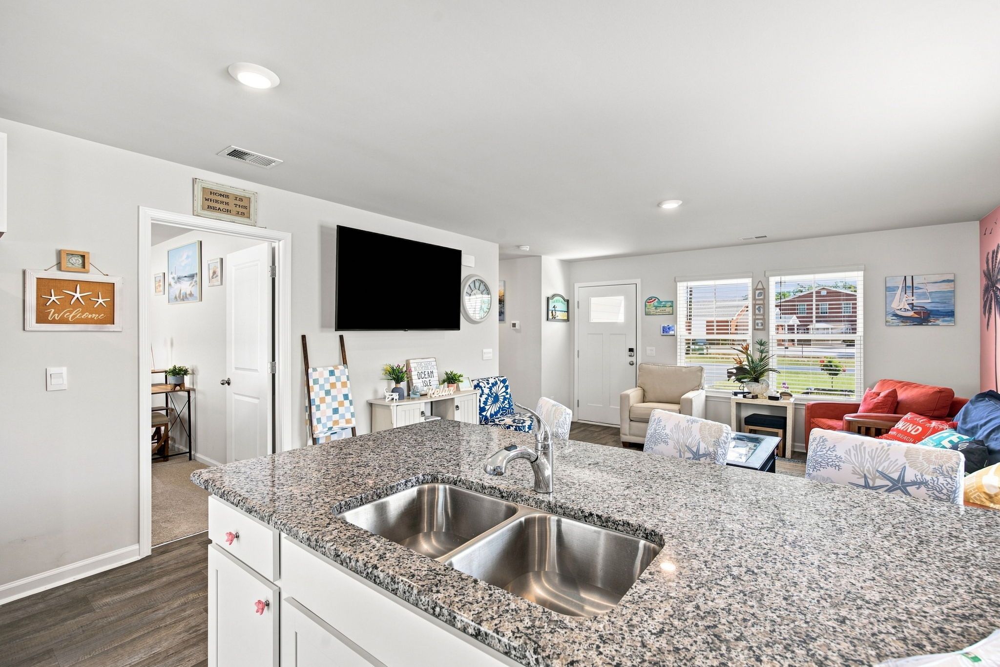 A modern kitchen with granite countertops and stainless steel sinks, a dining area with a table and chairs, and a living room with a sofa and a TV.