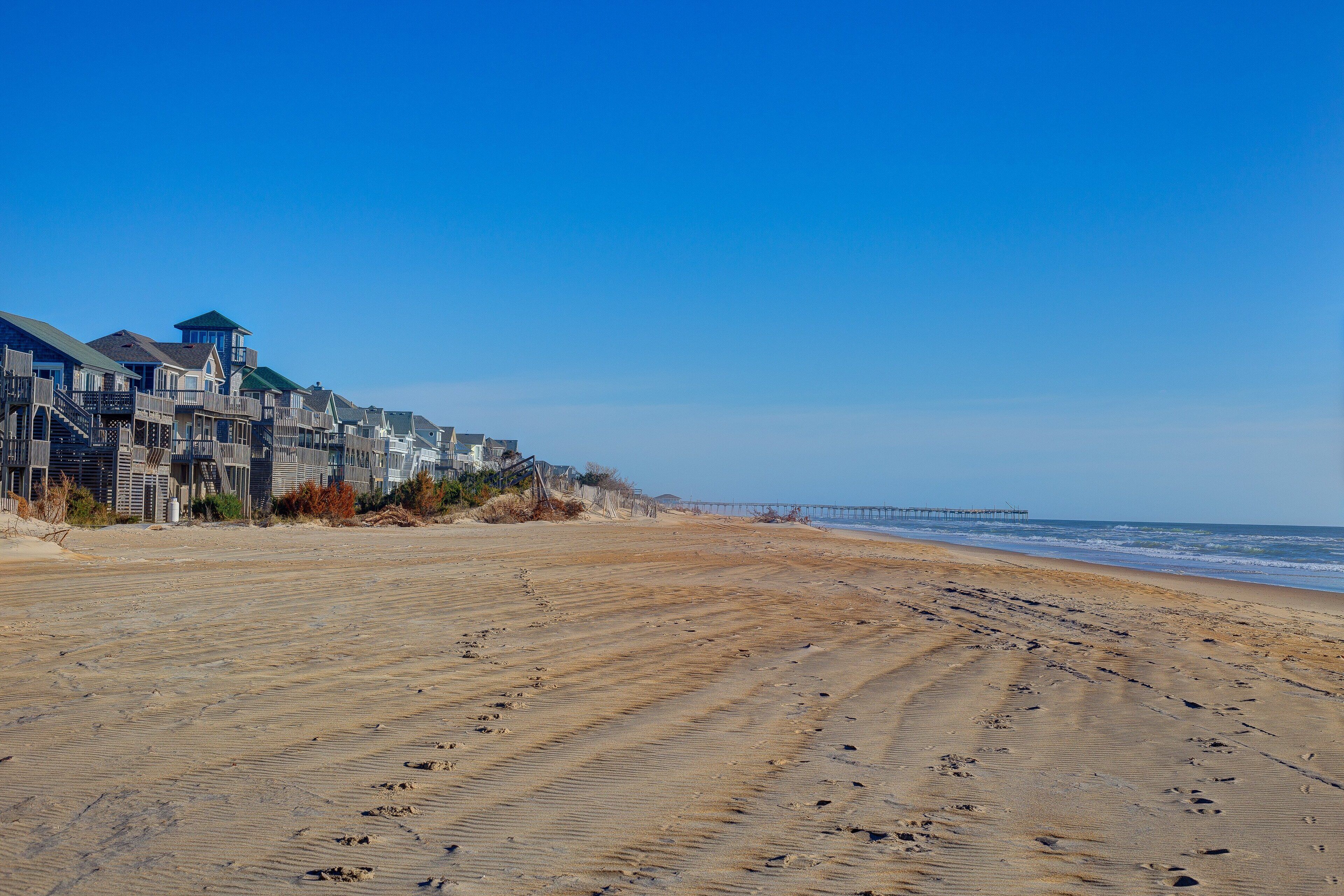 A beach with a row of houses and a pier in the background.