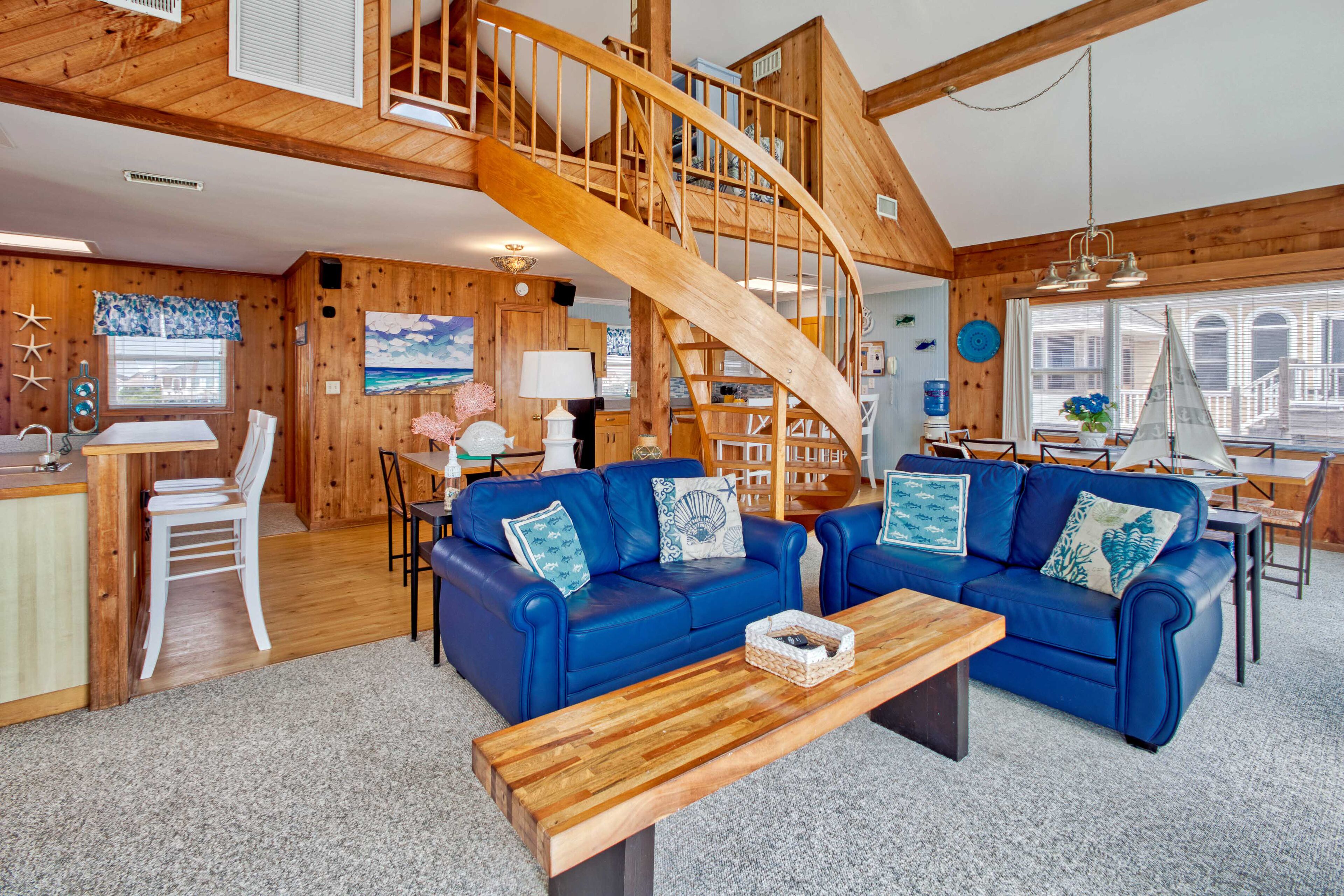 A spacious living area with a wooden staircase, blue sofas, and a wooden coffee table.