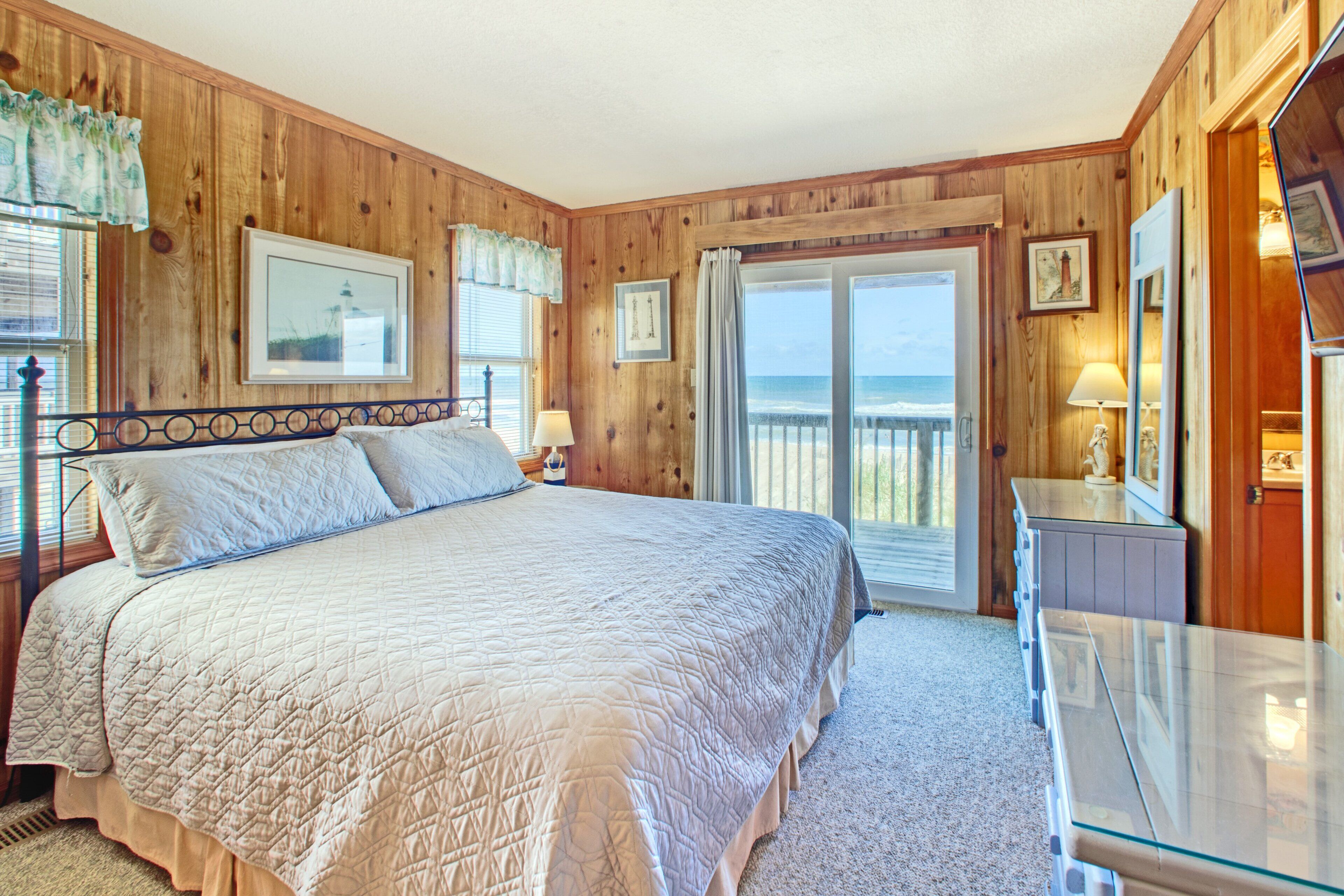 A bedroom with a large bed, wooden walls, a balcony with a view, and a glass table.