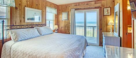 A bedroom with a large bed, wooden walls, a balcony with a view, and a glass table.