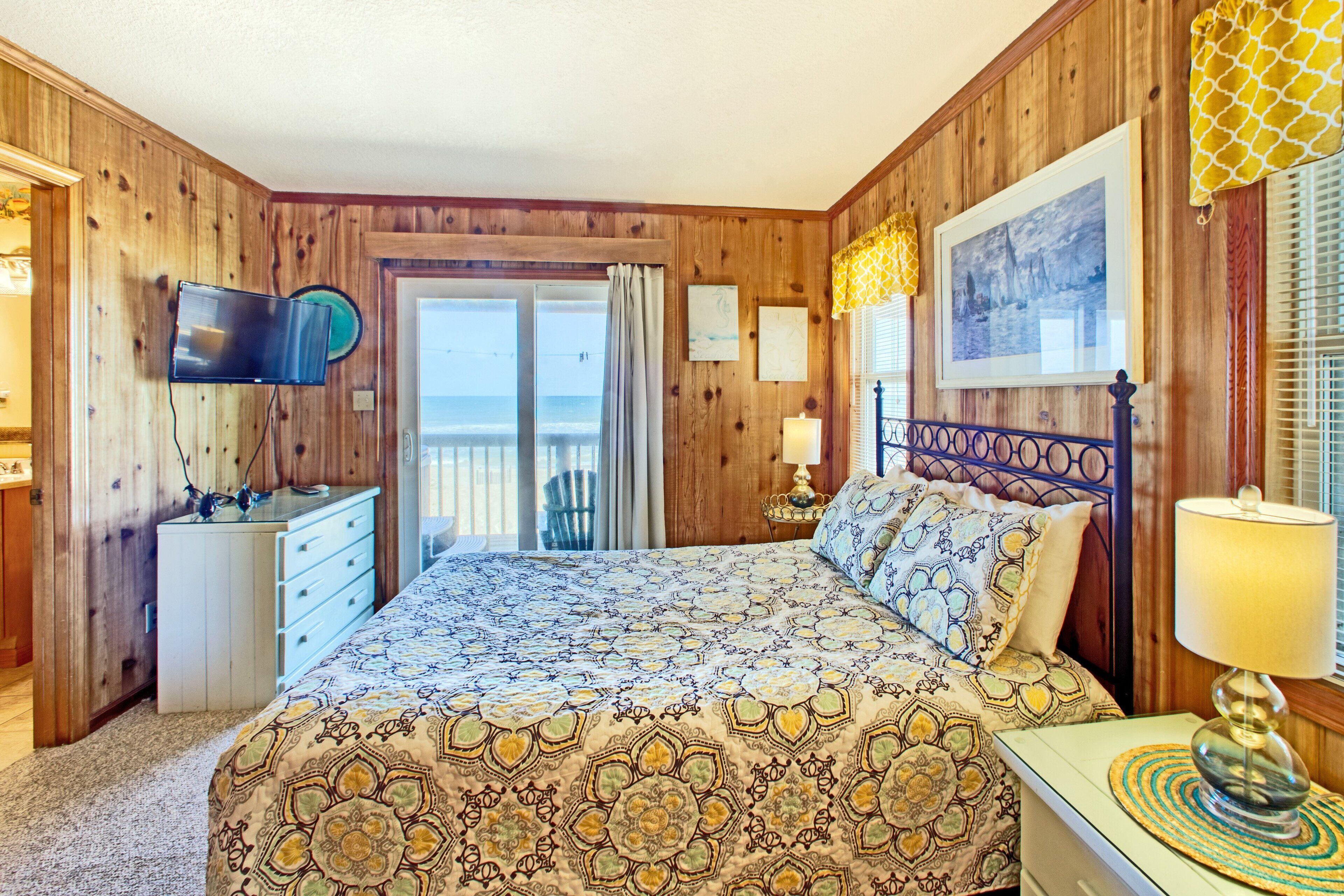 Camera da letto con rivestimenti in legno, un letto, una TV, una scrivania e un balcone.