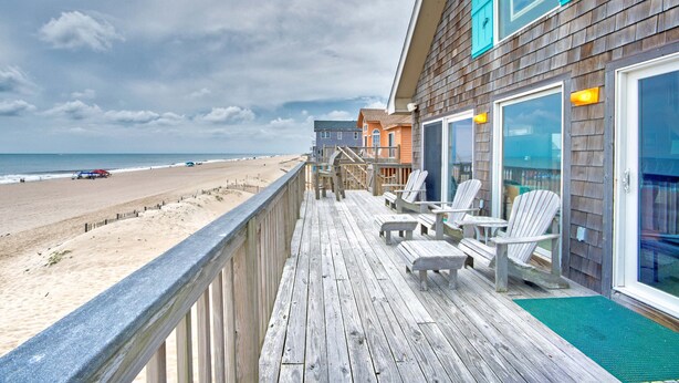 Eine Holzterrasse mit Stühlen und Blick auf den Strand.