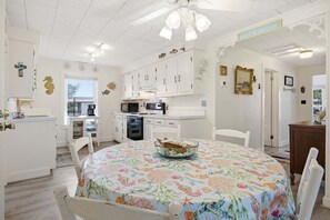Una cocina con armarios blancos, microondas y una mesa de comedor con mantel floreado.