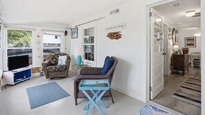 Ein gemütliches Wohnzimmer mit Fernseher, Korbmöbeln, einem blauen Tisch und einer Tür zu einem weiteren Raum.