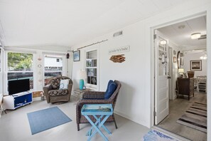 Una sala de estar acogedora con televisor, mobiliario de mimbre, una mesa azul y una puerta que da a otra habitación.