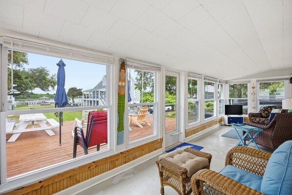 Un espacio al aire libre techado con mobiliario de mimbre, un televisor y vistas de la terraza y el exterior.