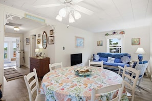 A room with a dining table, chairs, a blue sofa, a television, and a ceiling fan.