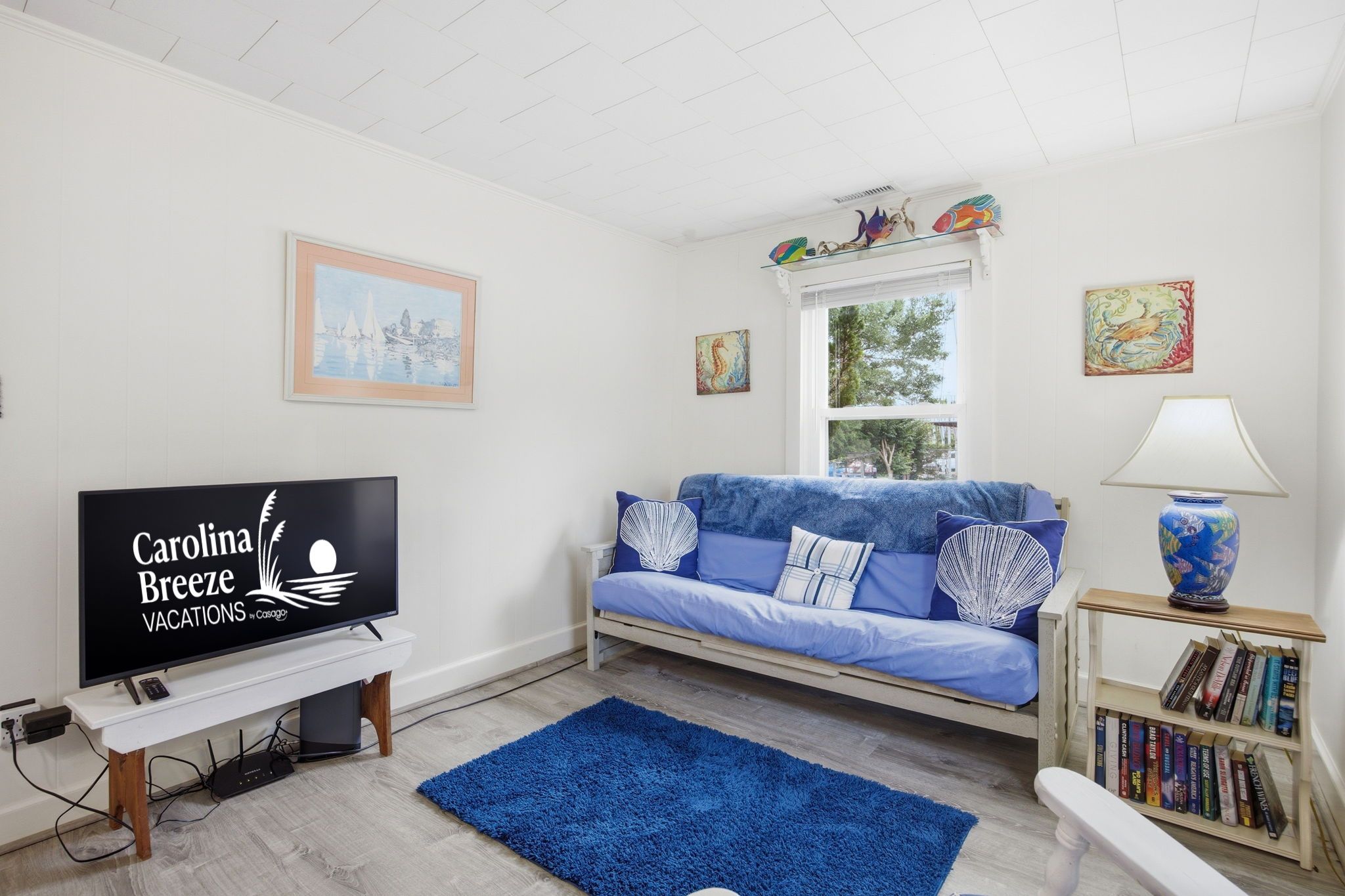 A living room with a television, sofa, bookshelf, and a window with artwork.