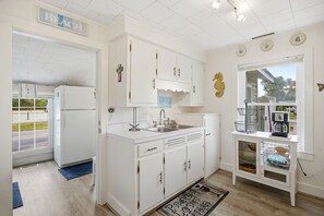 Una cocina con armarios blancos, un lavabo y una cafetera sobre una mesita.