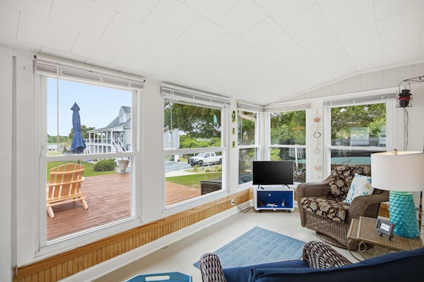 A sunroom with large windows, a TV, a sofa, and a wicker chair.